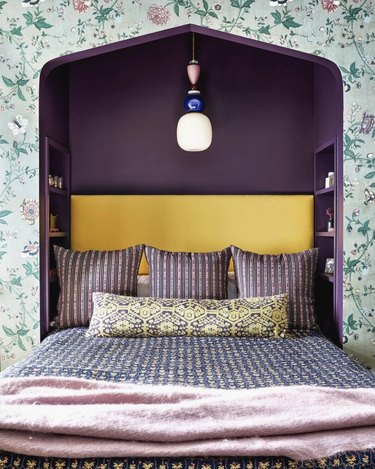 Bedroom with floral wallpaper and purple bedding.