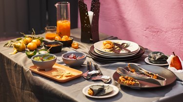 A table full of food and dishes from IKEA's ÖMSESIDIG collection. Guacamole, salsa, oranges and tortillas are shows, as well as a half-full pitcher, and a candle holder.