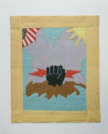 appliqué quilt design of a black fist holding a red lightning bold with a flag and sun nearby