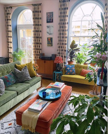 Eclectic living room with green sofa, red ottoman and pink walls.