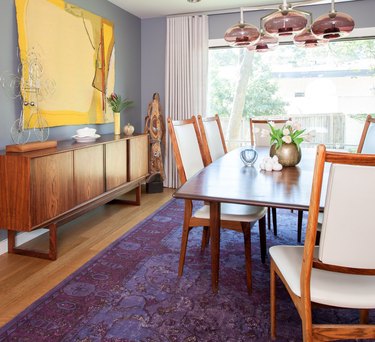 Dining room with yellow art, purple and lilac rug, lilac chandelier, dining set.