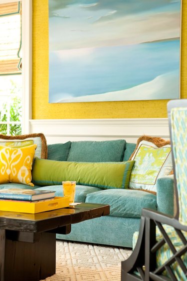 Living room with blue sofa, yellow walls and green throw pillows.