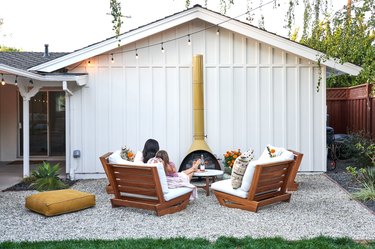 A woman and a child sit on a comfortable chair with their feet up on a small outdoor coffee table in front of an outdoor fireplace.