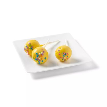 Yellow cake pops on a square white plate.