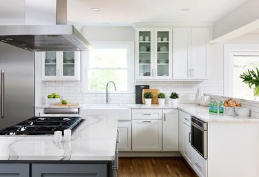Modern kitchen with large stainless hood, cooktop, white cabinets.