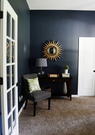 living room with navy walls, dark brown carpet, and gold sunburst mirror