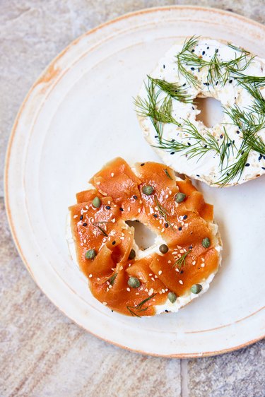 Plant-based lox on a bagel with capers on a white round plate.