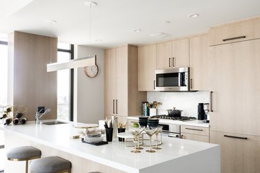 Modern kitchen with light wood cabinets, microwave, range, island.