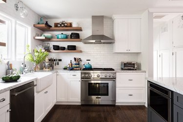White kitchen with stainless range, stainless hood, open shelves.
