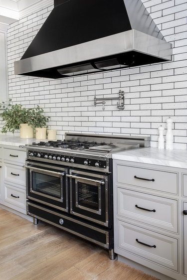 Kitchen with large black gas range, large black hood, white cabinets, subway tile.