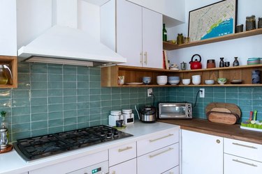 Kitchen with white cabinets, blue backsplash, white hood, open shelves.