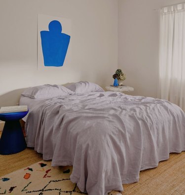 Bedroom with lilac sheets, royal blue artwork.