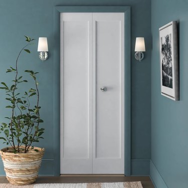 White bifold doors in a teal blue room; white sconces are on either side of the door and a large plant is to the left of the closet