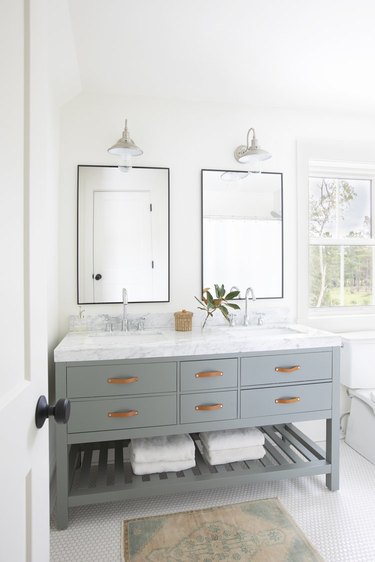 modern farmhouse bathroom idea with polished chrome barn lights, blue green cabinet with leather drawer pulls, marble countertop