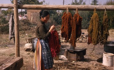Woman holding yarn with wooden structure holding other yarn bunches that are drying outdoors