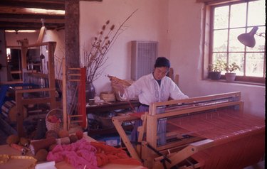 An archival photograph of a woman in a studio sitting in front of a weaving loom