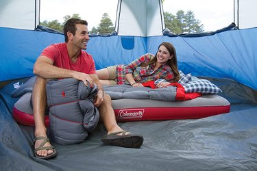 two campers in a blue tent sitting on a Coleman quickbed air mattress