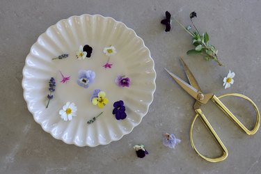 Assorted edible flowers on a white plate with gold scissors