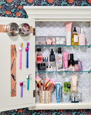 Medicine cabinet with wallpaper, makeup, toothbrushes and toothpaste.