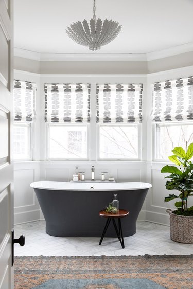 traditional bathroom with black tub surrounded by windows and paneling on the walls