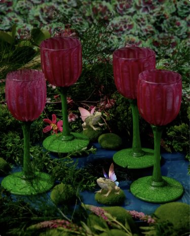 Four pink and green lotus-shaped wine glasses on a table set to look like a pond.