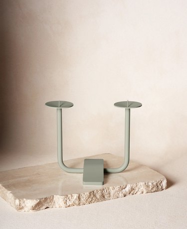 A sage green two-prong candleholder on a slab of cream-colored stone.