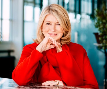Martha Stewart in a red sweater with a red scarf and her hand resting on her chin.