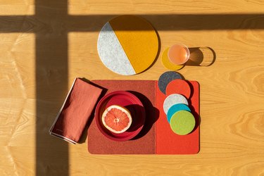 Colorful felt goods in different shapes and patterns on a light wood surface with shadow of window frame