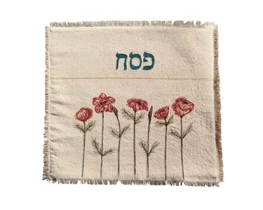A cream-colored matzah cover featuring anemone flowers along the bottom and fringe around the edge.