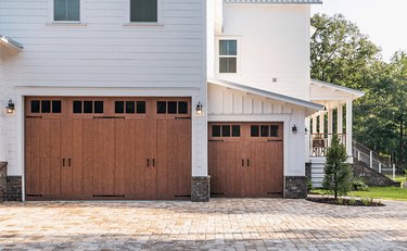 Two sets of wooden carriage garage doors on a white house