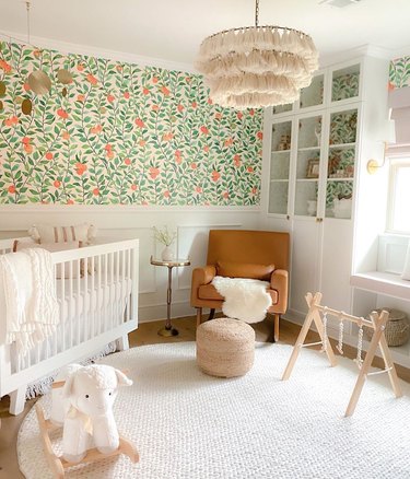 Nursery with citrus pattern wallpaper, tassle lamp, white crib, poof, chair.