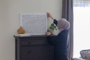 Summar Saad placing an artwork on her wood dresser