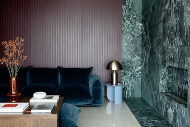 Living room with green marble fireplace, lavender paneled wall and deep blue velvet sofa.