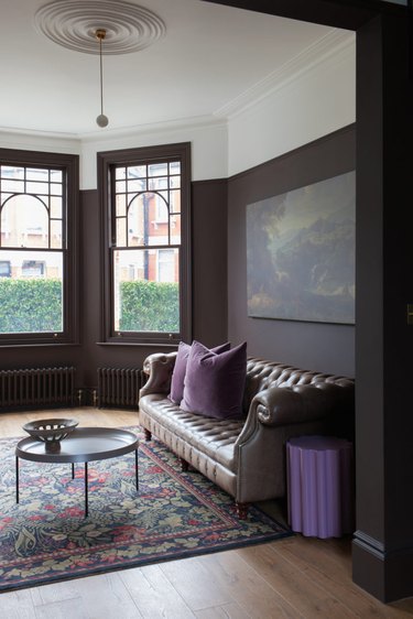 Sitting room with traditional architecture, painted brown walls, brown Chesterfield sofa, and green and purple accents.