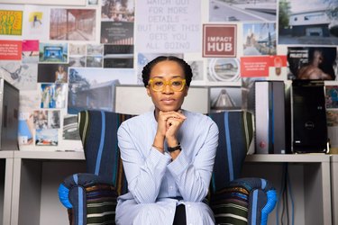 Tosin Oshinowo, a Black woman with pulled-black black hair, sitting in a chair in front of a wall covered in mood board images.