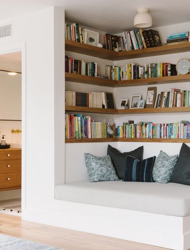 Modern home library with built-in shelves, built-in couch, books, light, pillows.