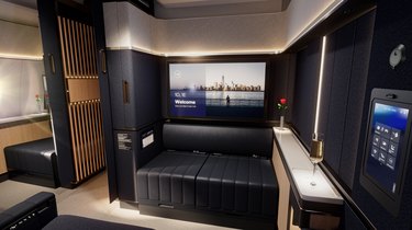 A seating room with a TV and leather couch in a small room on an airplane