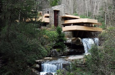 A large house built over a waterfall in the middle of the woods surrounded by green trees.