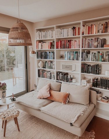 Home library with couch, books, pendant light, stool, pillows.