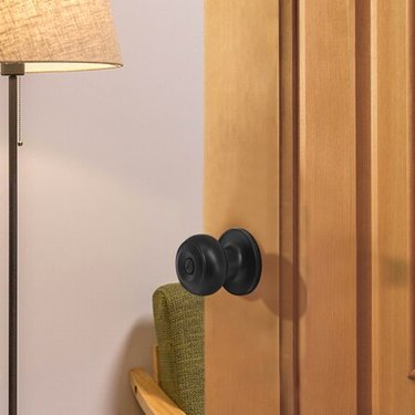 A black doorknob on a wood door; a lamp is in the background
