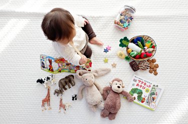 A small child surrounded by toys holding a small wood spoon in their mouth.