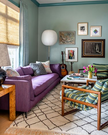 Living room with purple couch, seafoam green walls, striped chairs and Moroccan rug.