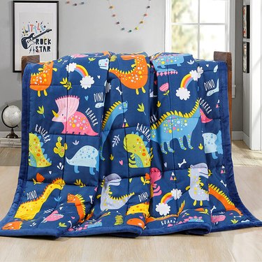 A weighted blanket with different-color dinosaurs and rainbows on it.