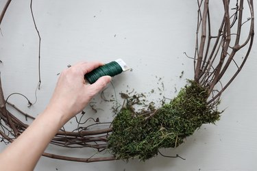 Wrapping sheet moss around grapevine wreath with floral wire