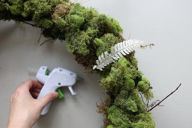 Gluing dried white fern to moss wreath