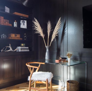 Dark charcoal gray millwork with built in book shelves, pampas grass, vase art, accent chair desk.