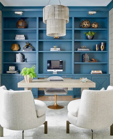 Blue built in book shelves, desk, chair, accent chairs, chandelier.