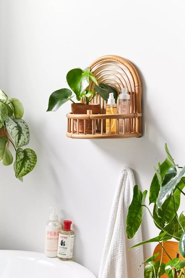 small boho bathroom with rattan wall shelf with plants next to a tub