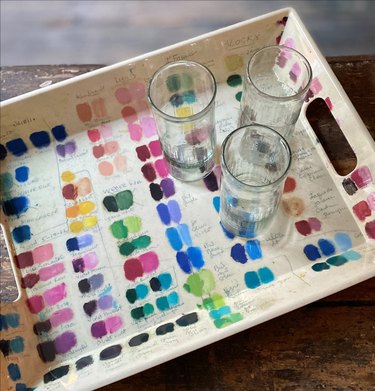 white tray with colorful paint swatches on it and three glasses. Tray sits on a wood table.