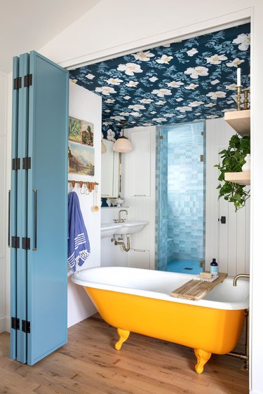 Maximalist bathroom with a yellow clawfoot tub, floral wallpapered ceiling and zellige tiled shower